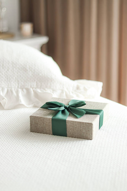 Святковий подарунок і розкішна онлайн доставка покупок, загорнута лляна подарункова коробка з зеленою стрічкою на ліжку в спальні, шикарний сільський стиль, крупним планом
 - Фото, зображення