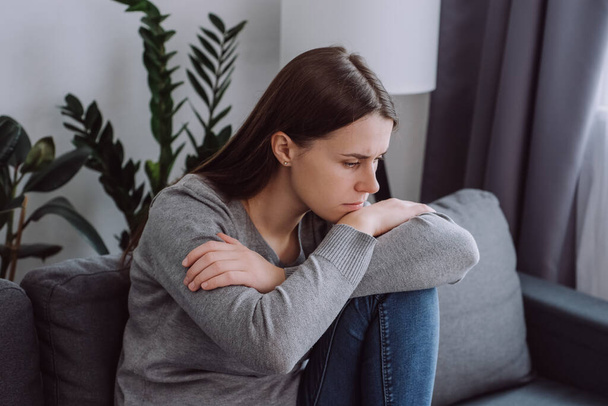 Close up of sad pensive young caucasian woman looking down depressed sitting on sofa in living room at home, thinking about personal problem, break up with boyfriend or divorce. Feeling lonely concept - Foto, imagen