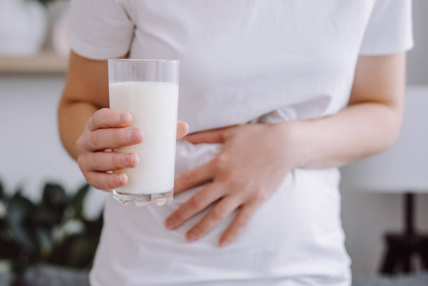 Крупным планом неузнаваемая нездоровая молодая женщина, держащая стакан молока, у которой болит живот из-за непереносимости лактозы. Проблемы со здоровьем молочных продуктов питания. Здравоохранение и медицина - Фото, изображение