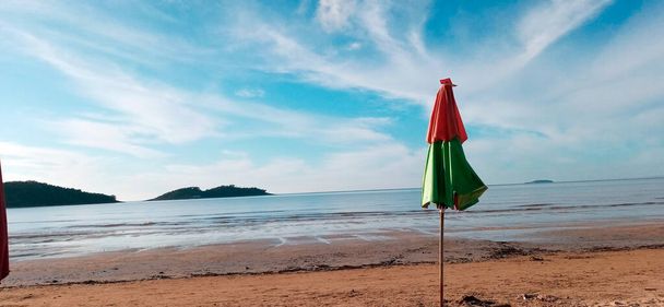 Umbrella, Parasol on Piuma beach with blue sky, dark sand, low tide waters and islands in the background. Espirito Santo, Brazil. One of the most frequented tourist spots on the south coast of the state of Esprito Santo, Southeast Region of Brazil. - Photo, Image