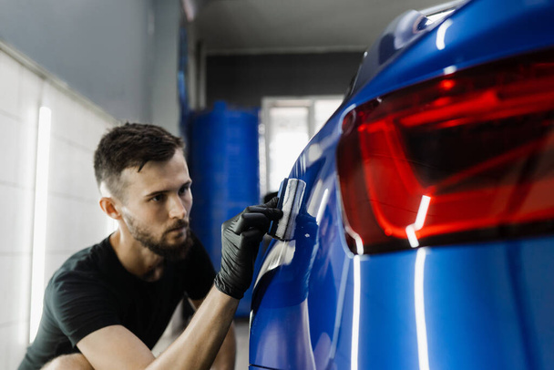 Ręczne nakładanie nanoceramicznego płaszcza ochronnego w celu ochrony samochodu przed zarysowaniami. Proces nakładania warstwy ceramicznej na karoserię przy użyciu gąbki w szczegółach serwisu samochodowego - Zdjęcie, obraz