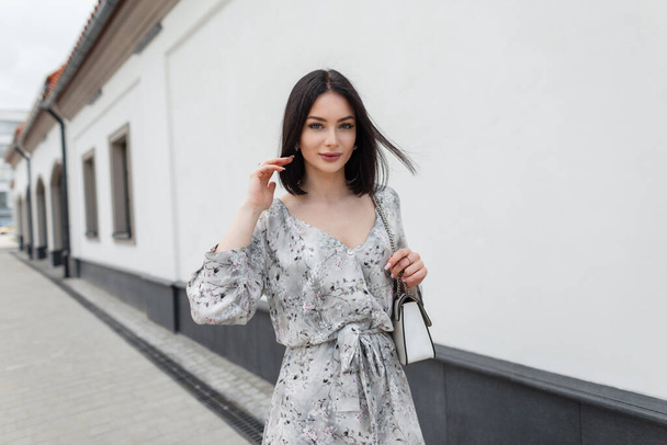 Элегантная модная модель с боб-стрижкой в стильном летнем цветочном платье с сумкой гуляет по городу - Фото, изображение