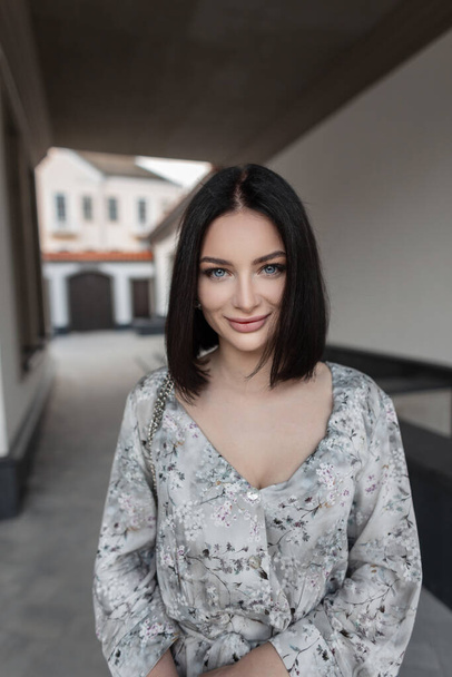 Elegant urban women's portrait of a beautiful happy girl with amazing blue eyes with a bob hairstyle in a fashionable vintage dress with a floral pattern with a bag walking and looking at the camera - Fotoğraf, Görsel