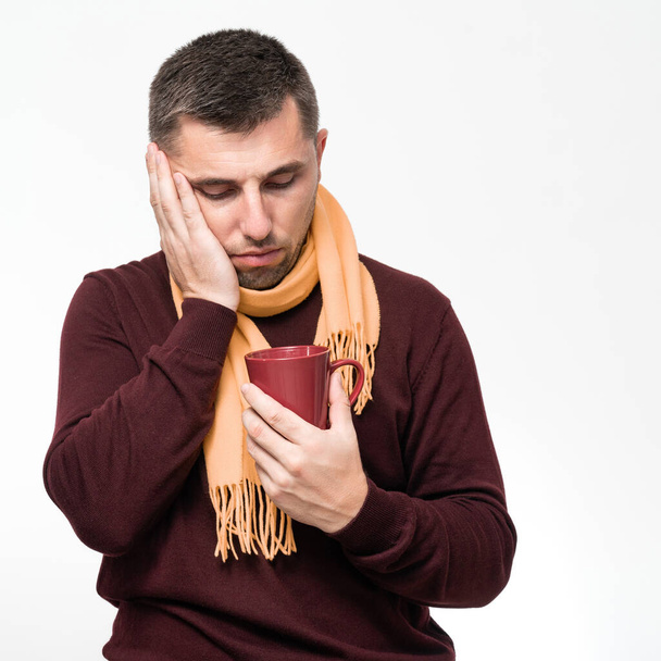 A handsome man touches his mouth with his hand with a pained expression because of a toothache or tooth disease, Dentist concept, a man wrapped in a scarf holds a mug in his hands. - Photo, image