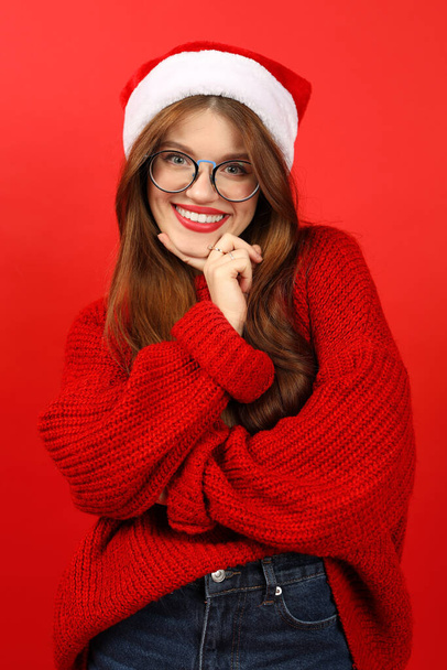 Smiling shy young woman portrait in red sweater and santa hat, vertical. - Photo, Image