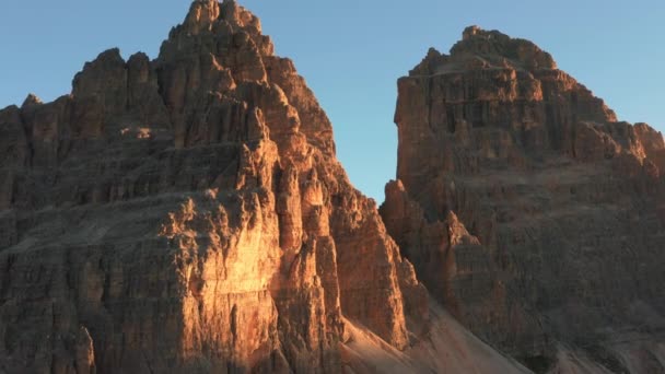 青い雲のない空の下で裸の岩の山々の範囲の記念碑的なギザギザのピーク。日の出時のTre Cime di Lavaredoの風景空撮 - 映像、動画