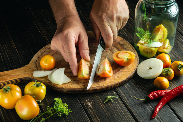 Las manos del cocinero cortan el tomate en la tabla de cortar de la cocina. Alimento campesino para preparar conservas en un frasco - Foto, Imagen