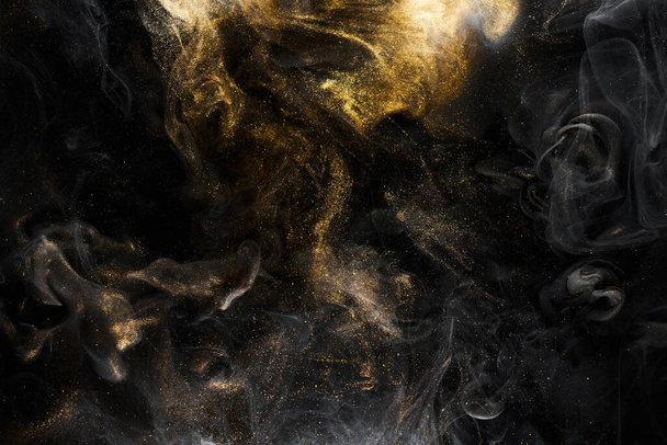 Golden sparkling abstract background, luxury black smoke, acrylic paint underwater explosion, cosmic swirling ink - Фото, изображение