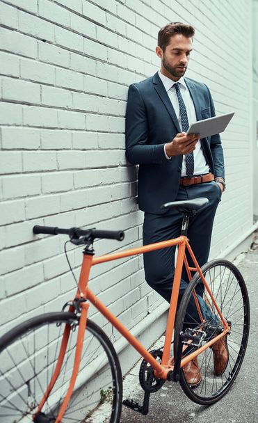 Kaupunkimaisema on hänen alaansa. komea nuori liikemies, joka käyttää digitaalista tablettia seistessään pyöränsä vieressä ulkona - Valokuva, kuva
