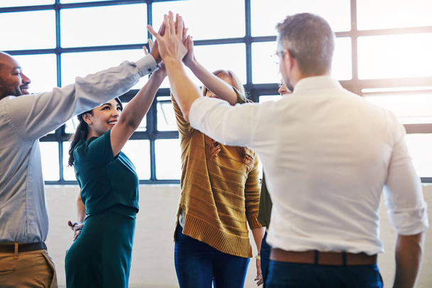 Succes is aan ons. Laten we het gaan halen. een groep collega 's die elkaar een high five geven in een modern kantoor - Foto, afbeelding