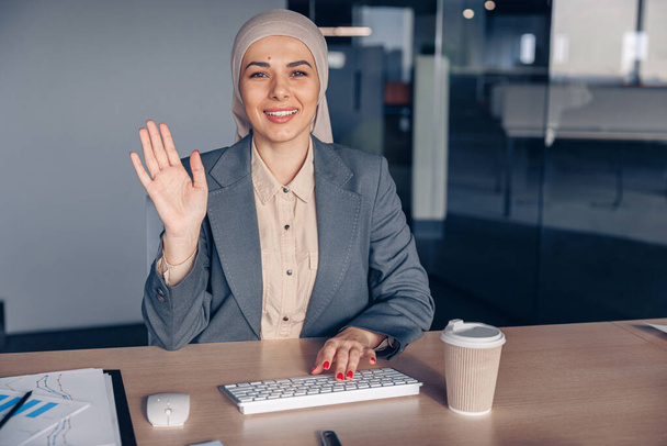 Modern ofiste çalışırken tesettürlü gülümseyen Müslüman iş kadını selam veriyor. Yüksek kalite fotoğraf - Fotoğraf, Görsel