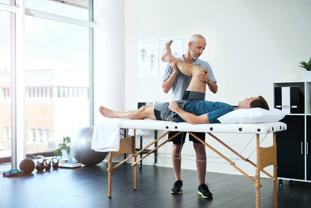 Hes got a gentle approach to rehabilitation. Full length shot of a handsome mature male physiotherapist treating a patient - Valokuva, kuva