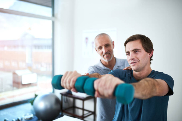 Strengthening those muscles for easier movement. a handsome mature male physiotherapist helping a patient work through his recovery with weights - Photo, Image