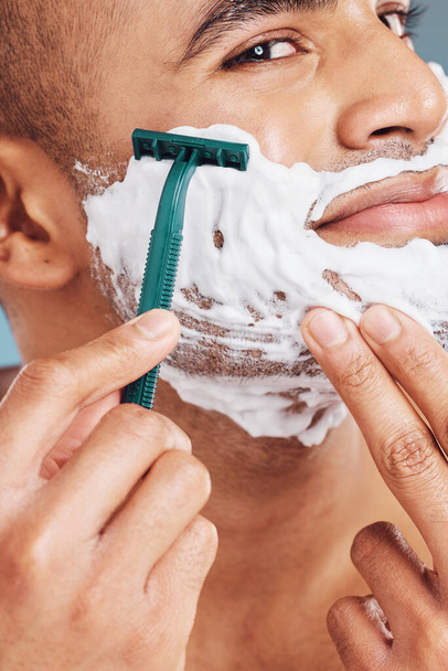 Ξυρισμένος, αφρός και άντρας ξυρίζει τα γένια του για υγιεινή, υγεία και απαλό δέρμα σε ένα στούντιο. Ξυράφι, καθαρός και όμορφος άντρας από την Ινδία που περιποιείται τα μαλλιά του προσώπου για δερματολογική ευεξία ή περιποίηση προσώπου - Φωτογραφία, εικόνα