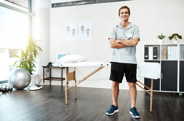 Welcome to my office. Portrait of a confident young male physiotherapist standing with his arms folded inside of his office - Фото, изображение