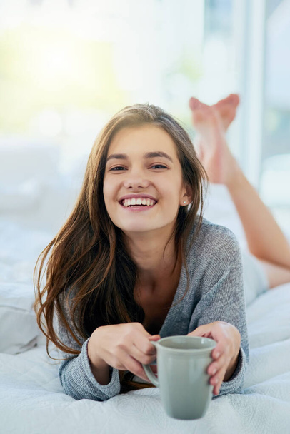 Beginnen Sie meinen Tag mit einer einfachen Note. Porträt einer attraktiven jungen Frau, die tagsüber Kaffee trinkt, während sie zu Hause auf ihrem Bett liegt - Foto, Bild