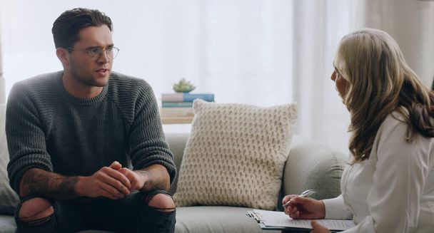 Therapy, man and therapist talking about mental health during a consultation in an office. Depression, communication and psychologist consulting with sad patient about anxiety or problem of the mind. - Photo, Image