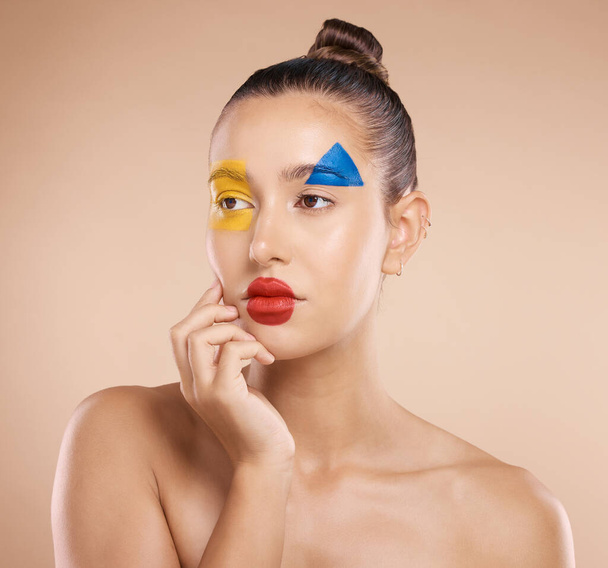 Beauty, art and portrait of woman paint on face, creative makeup and serious self expression. Skincare, creativity and hand touching cheek with artistic color shape cosmetics on young beautiful girl - Photo, Image