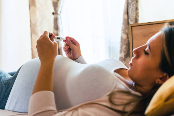 Pregnancy flu thermometer. Pregnant woman holding thermometer, check fever flu temperature. Pregnancy girl sick. Therapy, healthcare, motherhood concept - Φωτογραφία, εικόνα