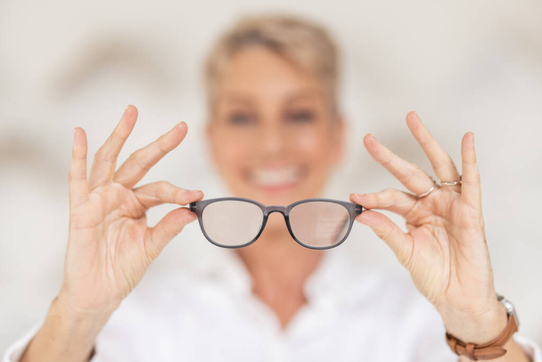 Vision, vue et lunettes dans les mains avec flou, la femme a une mauvaise vue en tenant des lunettes dans un fond flou. Soins de santé, assurance médicale et des yeux, lentille de prescription dans des montures de lunettes claires. - Photo, image