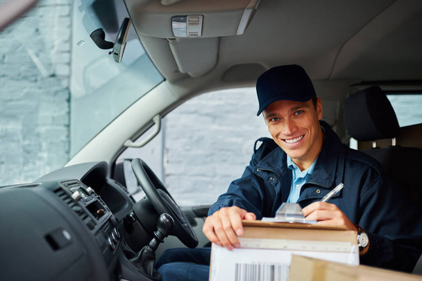 Making sure I have all my customers packages ready. a handsome young delivery man using a clipboard - Foto, Imagen