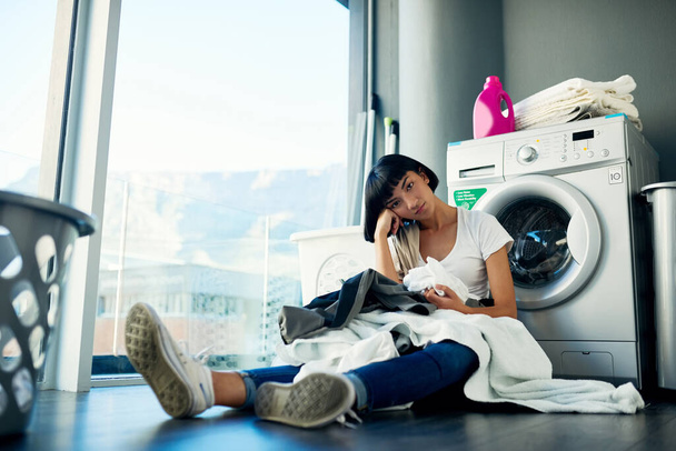 Do I really have to do this myself. an attractive young woman looking bored while doing the laundry at home - Valokuva, kuva