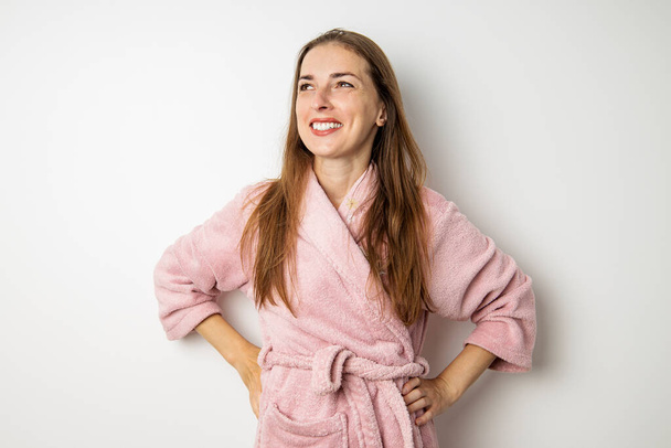 Smiling young woman in a pink bathrobe on a white background. - Photo, image