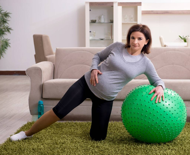 Беременная женщина в возрасте делает упражнения дома
 - Фото, изображение