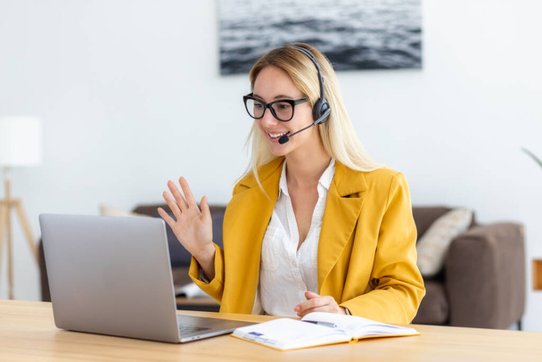 Young woman in headset having in video meeting communicates with employees or the client online using laptop computer. Smiling female agent or support worker consults a client - Φωτογραφία, εικόνα