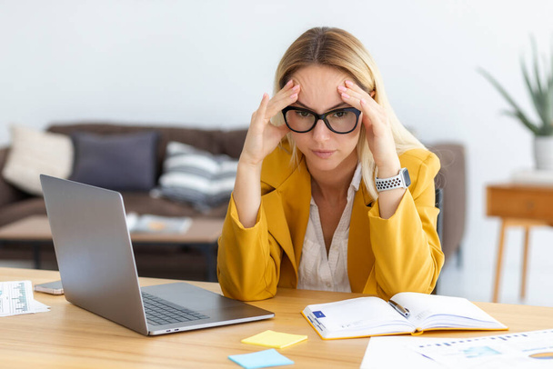 Tired stressed caucasian businesswoman having headache, feeling sick, pain, depression, overwork concept. Woman entrepreneur experiencing financial crisis at work - 写真・画像