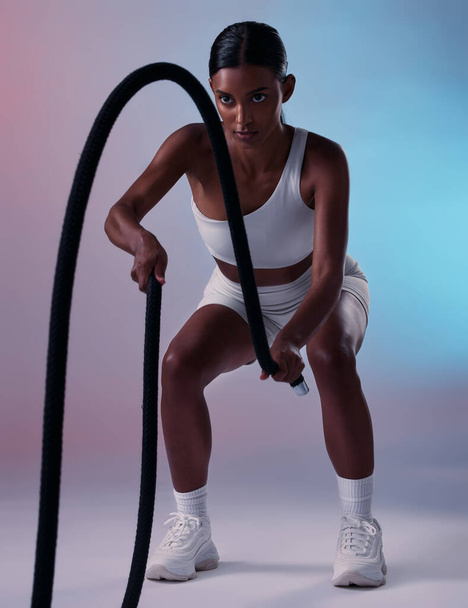 Girl, fitness and rope training exercise for cardio, muscle and endurance practice with color studio background. Focus, health and power of Indian woman training with gym wellness workout gear - Foto, Imagen