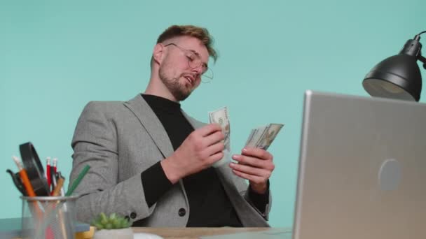 Rikas tyytyväinen liikemies istuu toimistopöytä heiluttaa rahaa dollarin seteleitä laskuja kuin fani, menestys liike-elämän ura, arpajaiset voittaja, suuret tulot, rikkaus. Nuori pomo kaveri sinisellä taustalla - Materiaali, video