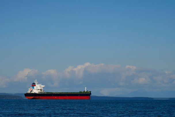 Ένα μεγάλο κόκκινο και μαύρο φορτηγό πλοίο στη μέση του λιμανιού περιμένει να ξεφορτώσει το φορτίο του.  - Φωτογραφία, εικόνα