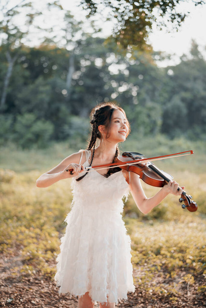 La chica está tocando el violín bajo el gran árbol - Foto, Imagen