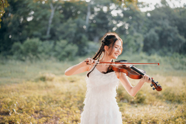 The girl is playing the violin under the big tree - Фото, зображення