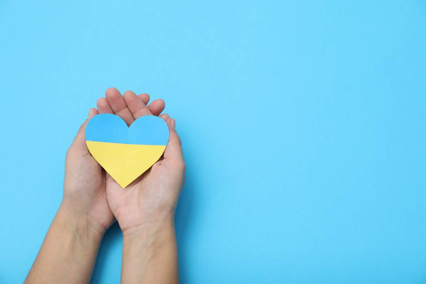 Woman holding paper heart in colors of Ukrainian flag on light blue background, top view. Space for text - Valokuva, kuva