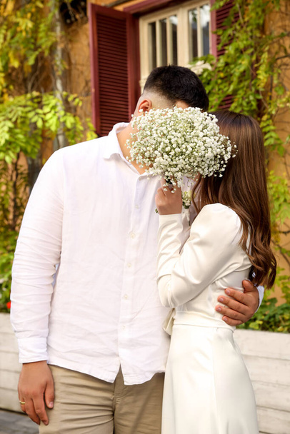 Bride and groom kissing behind bouquet of flowers on wedding day - Foto, afbeelding