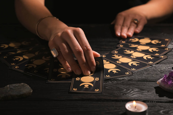 Soothsayer predicting future with tarot cards at table in darkness, closeup - Fotografie, Obrázek
