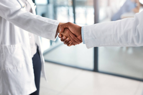 Samenwerking is goed voor iedereen. Close-up van twee onherkenbare dokters die elkaar de hand schudden in een ziekenhuis - Foto, afbeelding