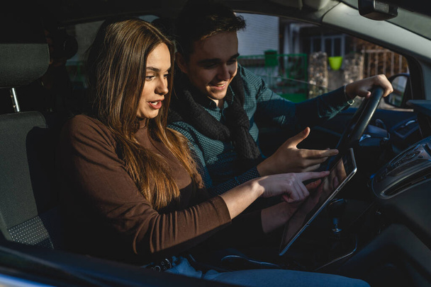 Man and woman young couple or friends male and female boyfriend and girlfriend using digital tablet for navigation searching map for direction while travel in car real people copy space - 写真・画像