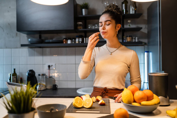 One woman young adult happy caucasian female smile while cutting and eating fruit at the kitchen counter in the morning healthy eating vegan and vegetarian concept real people copy space - Photo, image