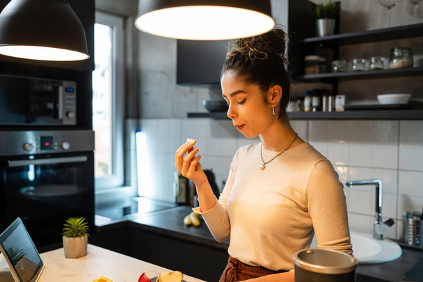 One woman young adult happy caucasian female smile while cutting and eating fruit at the kitchen counter in the morning healthy eating vegan and vegetarian concept real people copy space - Foto, Bild