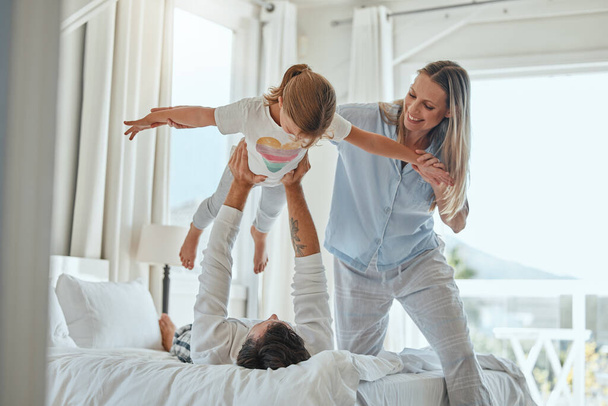 Family, mother and father lifting girl, playing and bonding in home bedroom. Love, support and happy man and woman holding child up in air, enjoying quality time together and having fun in house - Фото, зображення