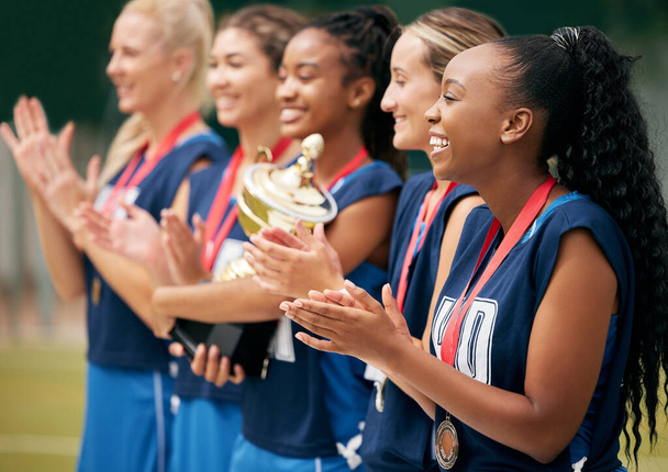 Trophy, sports and women clapping hands for success, motivation or celebration at professional netball game. Winning, support and athlete team with trust, support and smile to celebrate win in sport. - Photo, Image