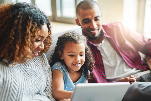 Tomar la tecnología como algo natural. una adorable niña y sus padres usando una tableta digital juntos en el sofá en casa - Foto, Imagen