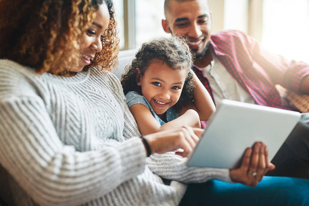 Recibiendo mi primera lección de seguridad en línea. una adorable niña y sus padres usando una tableta digital juntos en el sofá en casa - Foto, Imagen