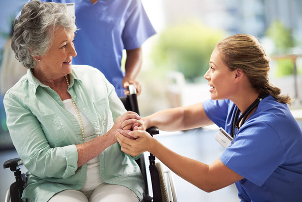 Estás en buenas manos con nosotros. un médico cogido de la mano con una mujer mayor en silla de ruedas - Foto, Imagen