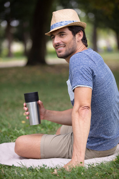 young man sitting outdoors in the park holding hot coffee - Fotó, kép