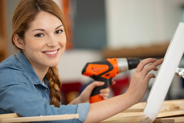 female worker using orange drill on wooden pieces - 写真・画像
