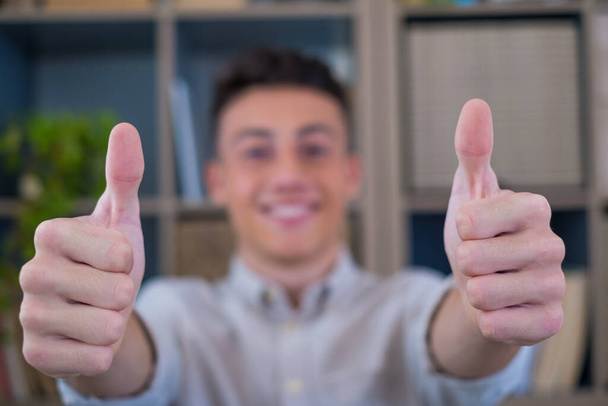 Close up focus on male hand with thumbs up gesture. Smiling attractive young caucasian man employee recommending good service, satisfied with successful career in international company.  - Photo, Image